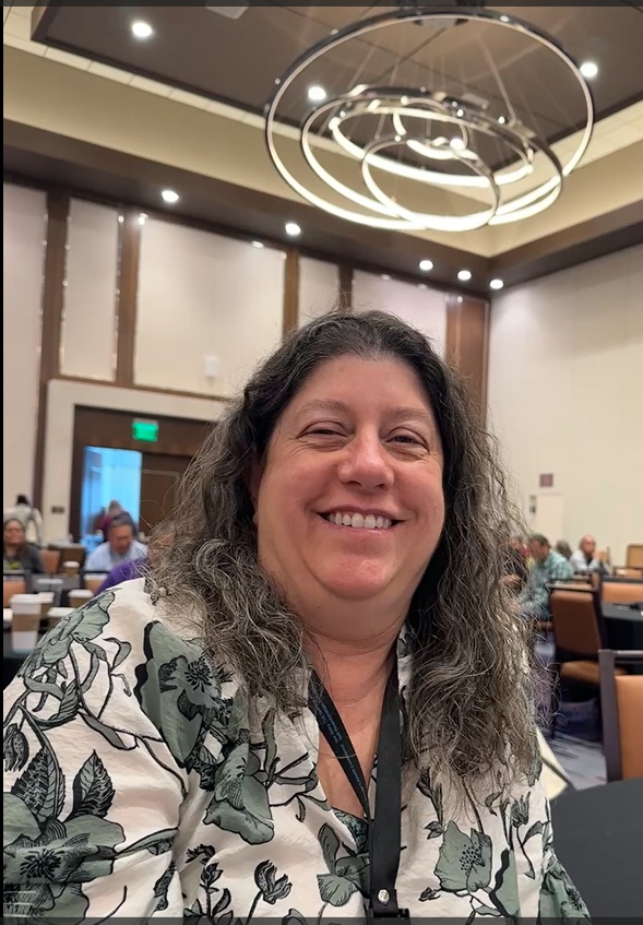 Beth smiling and seated at a conference.
