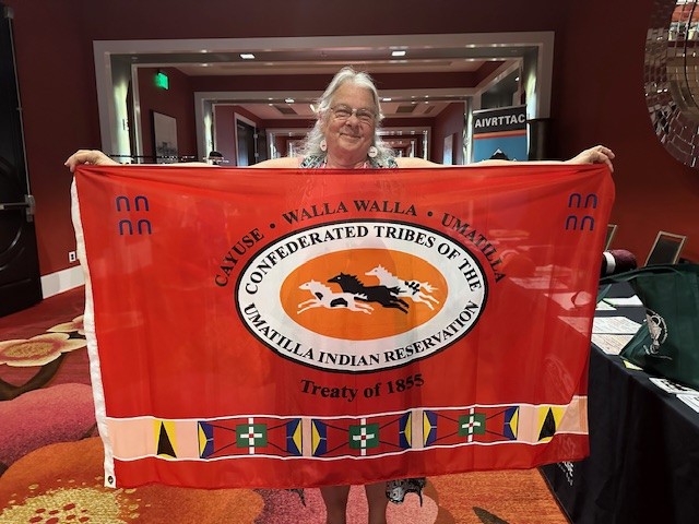 Woman holding flag with the logo for Confederated Tribes of the Umatilla Indian Reservation.